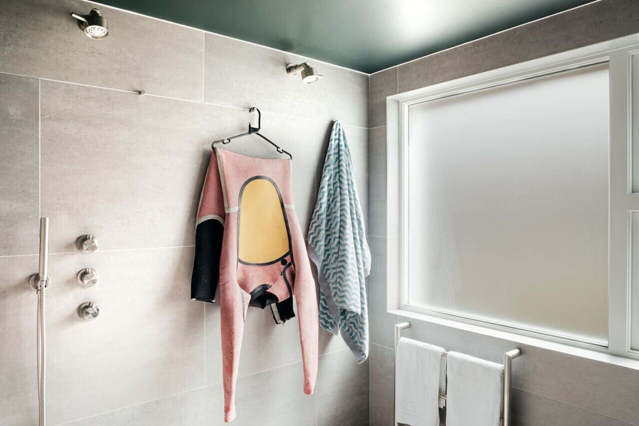 Une salle de bain avec une douche, un porte-serviettes avec une serviette rose et une serviette à motifs, et une porte blanche.
