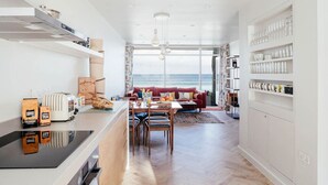 A modern kitchen with a dining area, a red sofa, and a view of the sea.