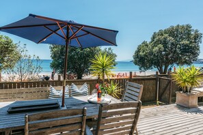 Une terrasse en bois avec une table et des chaises, un grand parasol et une vue sur la plage et l’océan.