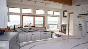 A modern kitchen with large windows, a marble countertop, and a view of the sea.