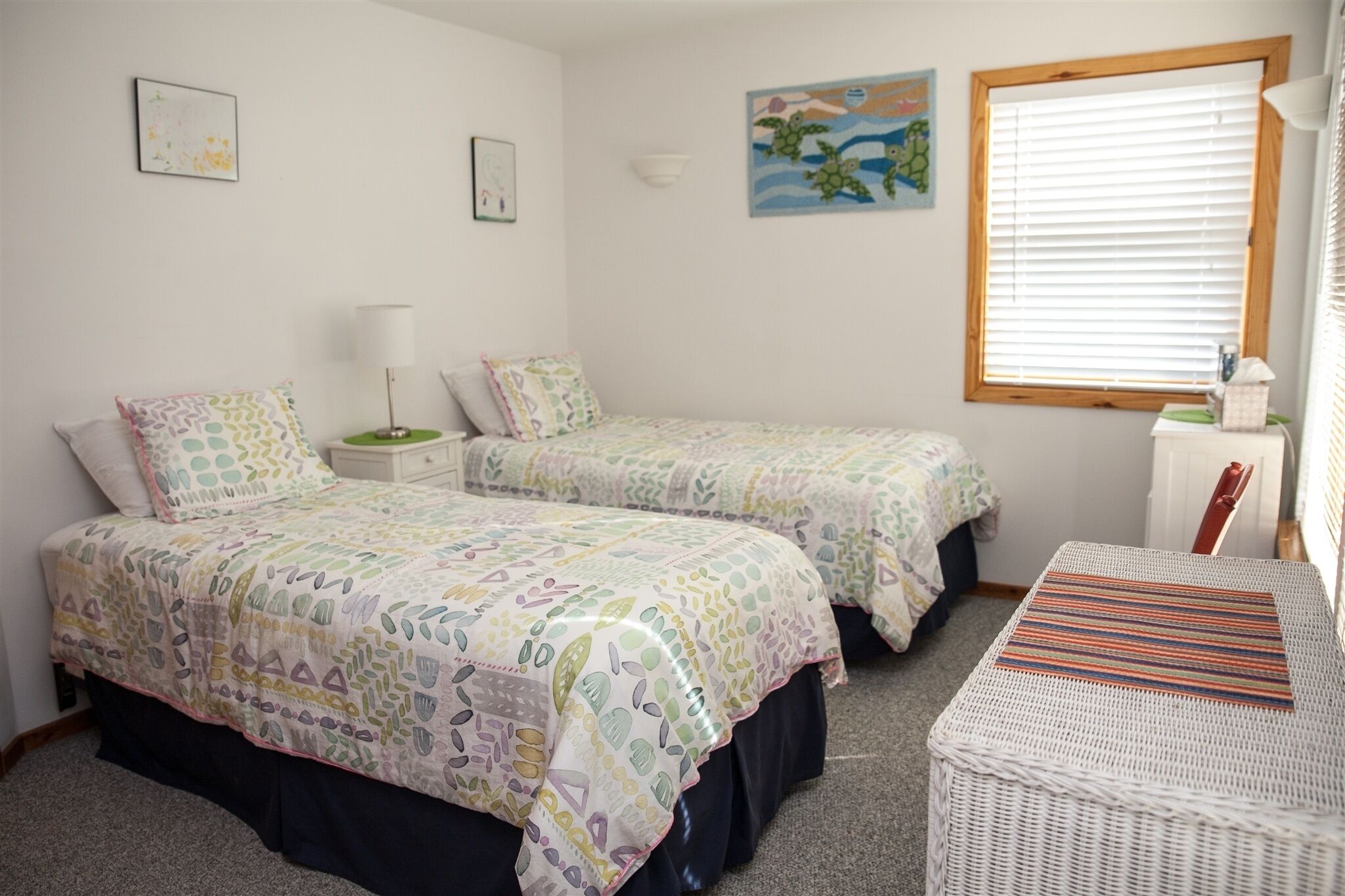 A bedroom with two beds, a small table, a chair, and a window with blinds.