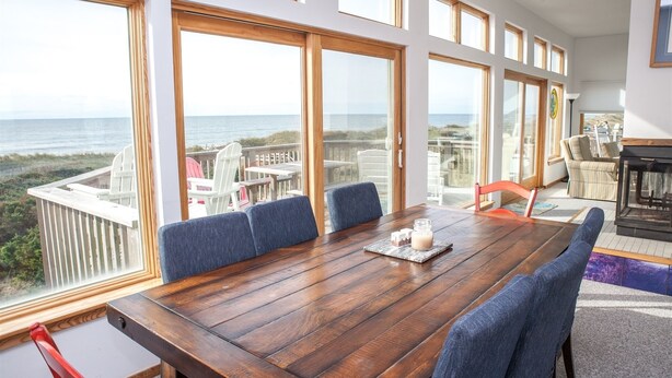 A spacious room with a large wooden table, blue upholstered chairs, and a view of the ocean through large windows.
