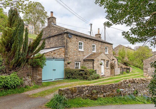 A stone building with a blue door, surrounded by greenery and a stone wall.