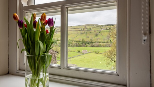 Ein Fenster mit Blick auf ein grünes Feld und eine Steinmauer.