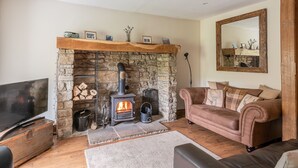 Ein gemütliches Wohnzimmer mit Kamin aus Stein, einer Couch, einem Fernseher und einem Holzbalken an der Decke.