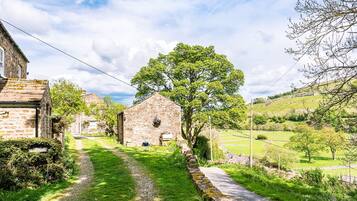 Un edificio de piedra con techo de paja, un sendero estrecho y un gran árbol en primer plano.