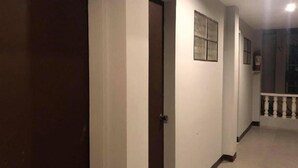 Un pasillo con una puerta cerrada, un ventanal y una escalera con barandilla.