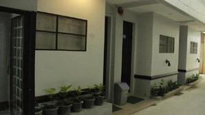 Fachada de edificio con varias ventanas, una puerta y numerosos maceteros a lo largo del acceso.