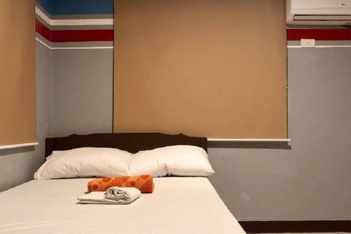 Una habitación de hotel con una cama, almohadas, una toalla doblada y una manta naranja.