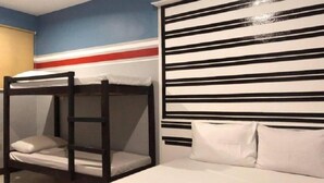 Una cama litera con colchón y almohadas blancos, estructura de madera y una pared con rayas horizontales negras y blancas.