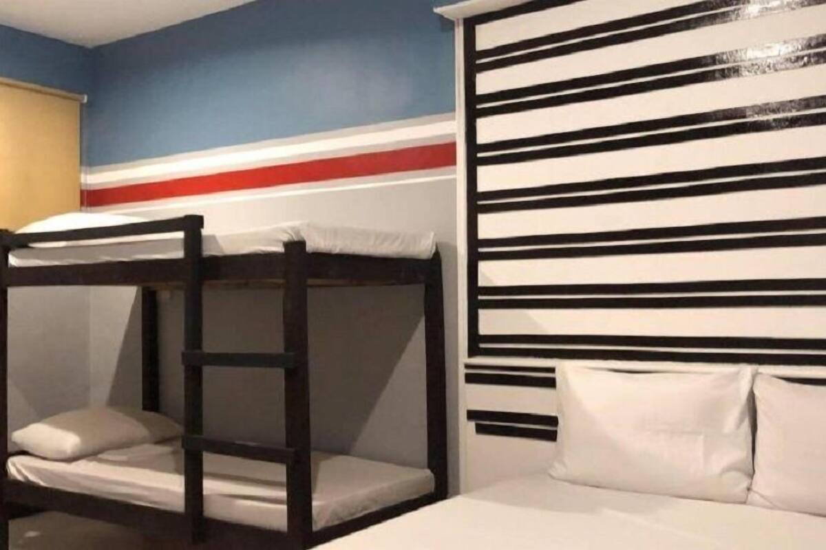 Una cama litera con colchón y almohadas blancos, estructura de madera y una pared con rayas horizontales negras y blancas.