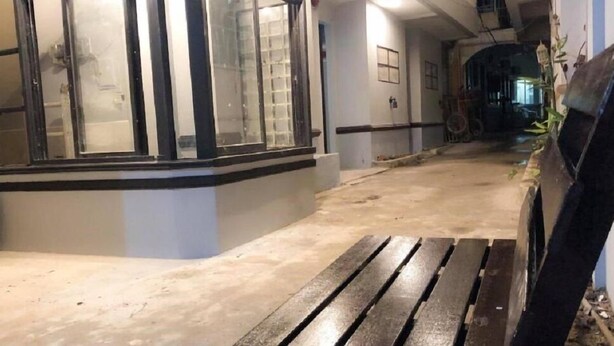 Un pasillo con un banco, suelo de baldosas y entrada a un edificio con puertas de cristal.