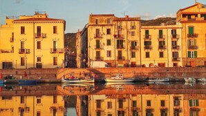 A waterfront with buildings reflected in calm water, a small boat docked, and a clear sky.