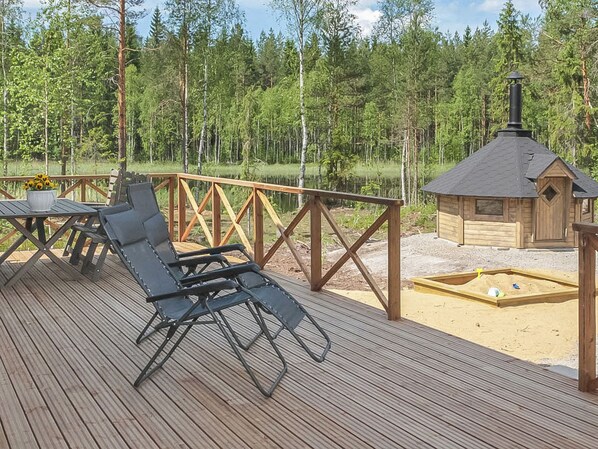 A wooden deck with a metal grill, a small wooden structure, and a forested background.