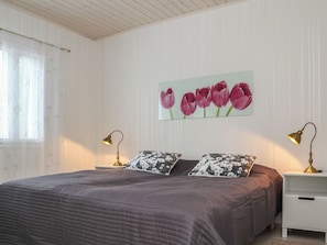 Un dormitorio con cama, dos lámparas de noche, una ventana con persianas y un cuadro de tulipanes colgado en la pared.