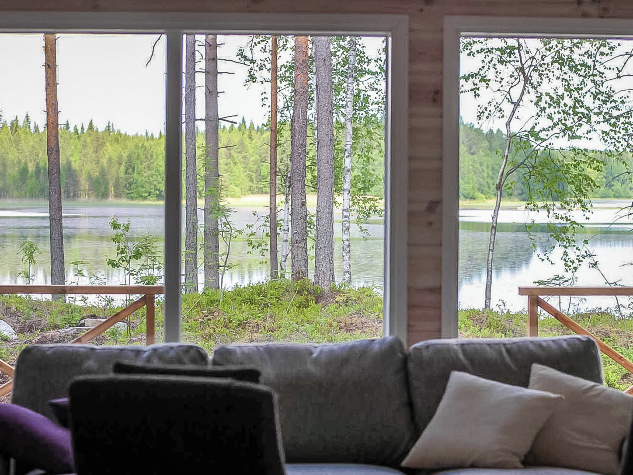 A room with a sofa facing a large window overlooking a lake and forest.