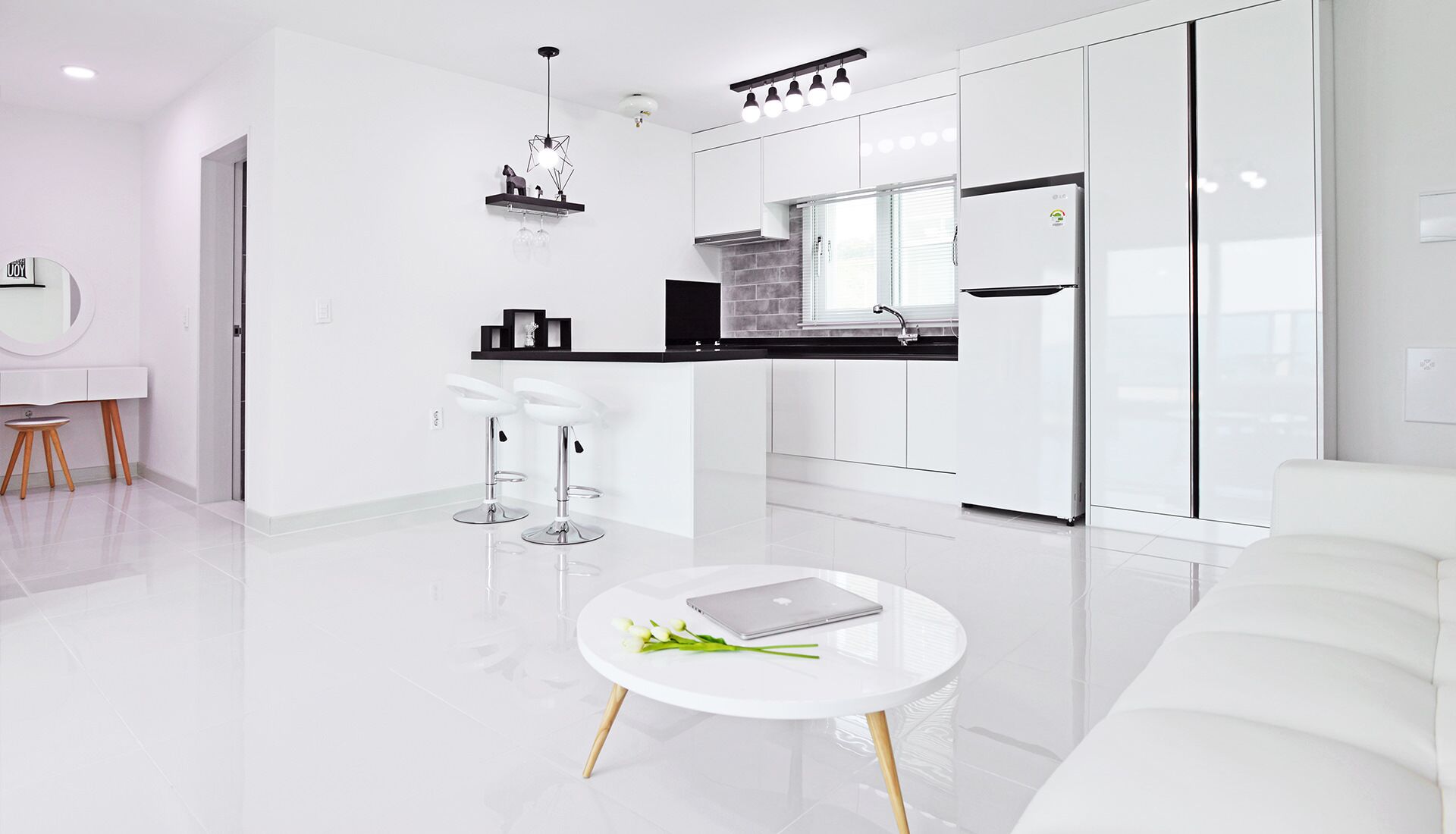 A modern kitchen with white cabinets, a black countertop, and a built-in oven. There is a white dining area with a round table and two bar stools.