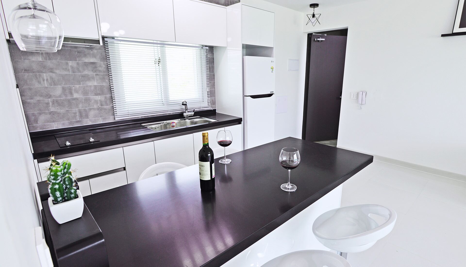 Una cocina moderna con encimera oscura, armarios blancos, horno empotrado y una botella de vino con una copa.
