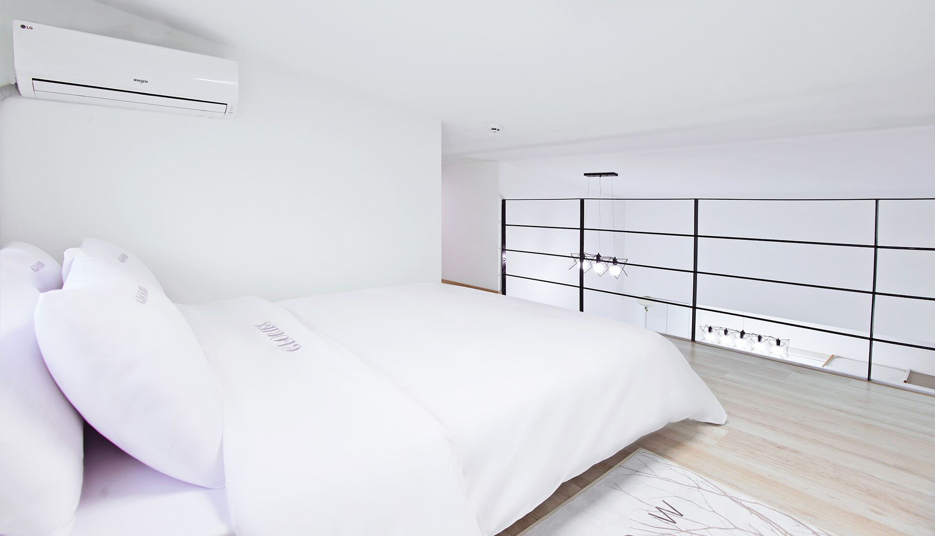 Un dormitorio minimalista con cama, ropa de cama blanca, armario empotrado y aire acondicionado.