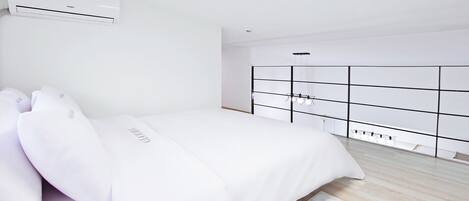 Un dormitorio minimalista con cama, ropa de cama blanca, armario empotrado y aire acondicionado.
