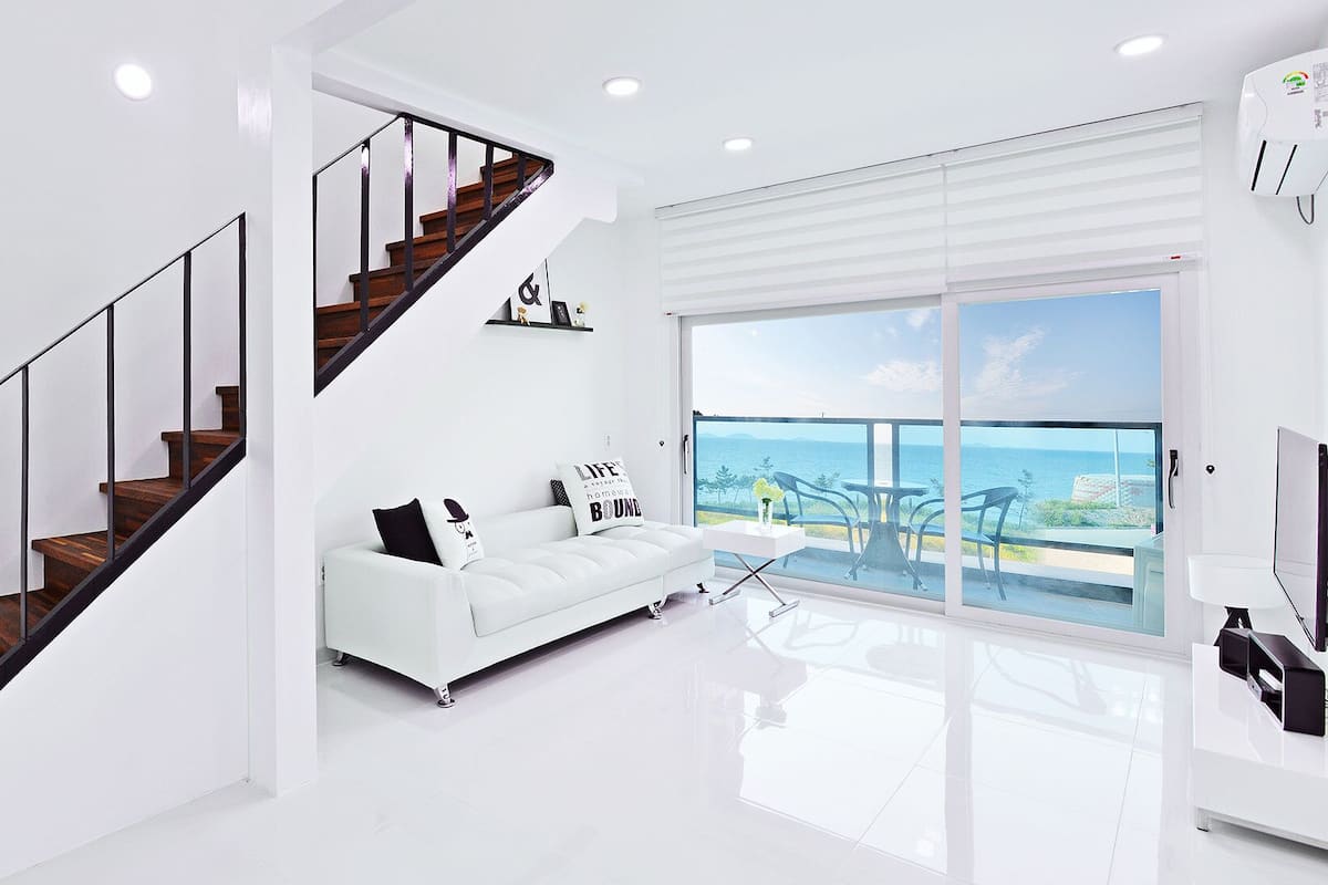 A modern living room with a white sofa, a coffee table, and a view of the sea through large windows.