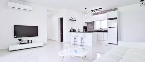Una sala de estar moderna con una televisión de pantalla plana, un sofá blanco y una zona de comedor con dos taburetes de bar.