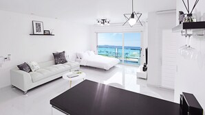 A modern, minimalist bedroom with a white sofa, a bed, and a large window offering a view of the sea. - Glories Pension (Buan)