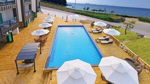 A swimming pool with lounge chairs and umbrellas, surrounded by a wooden deck and overlooking a coastal area. - Glories Pension (Buan)