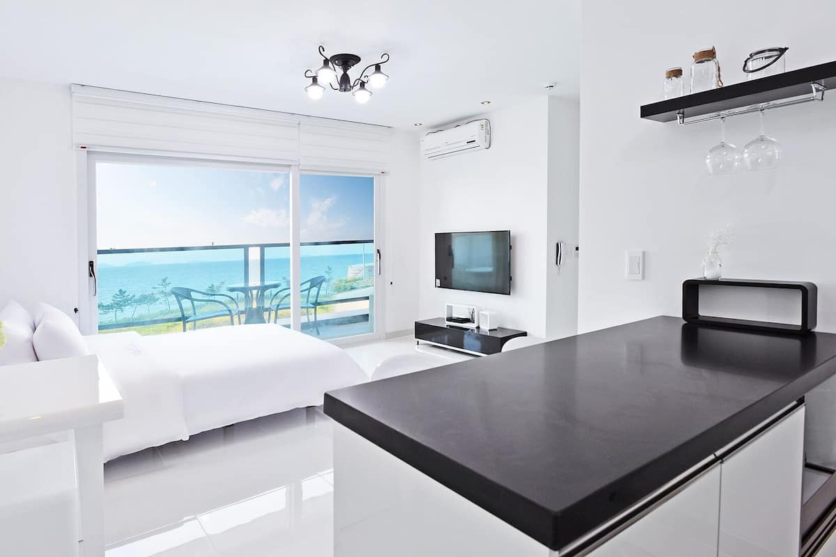 A modern hotel room with a balcony, a flat-screen TV, a dining area, and a minimalist design.