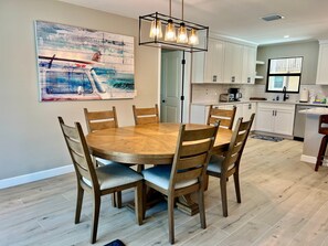 A modern kitchen with white cabinets, a wooden dining table with six chairs, and a pendant light fixture.