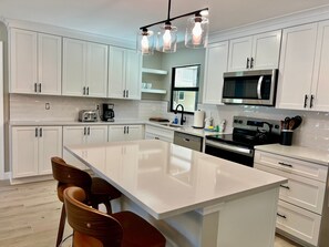 A modern kitchen with white cabinetry, a central island, a microwave, and a coffee maker.