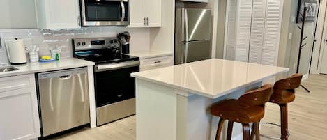 A modern kitchen with white cabinets, stainless steel appliances, a central island, and two wooden bar stools.