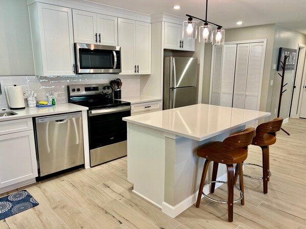 A modern kitchen with white cabinets, stainless steel appliances, a central island, and two wooden bar stools.