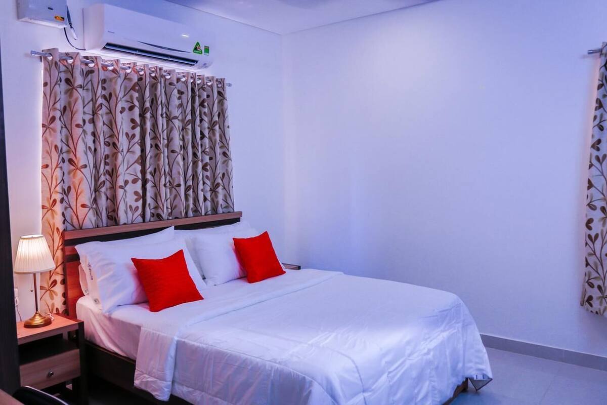 A hotel room with a bed, a nightstand, a lamp, and a wall-mounted air conditioner.