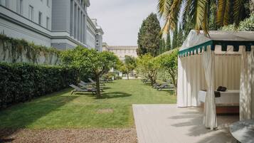 Une cour avec un lit placé sous un auvent, des fauteuils de relaxation et un bâtiment en arrière-plan.