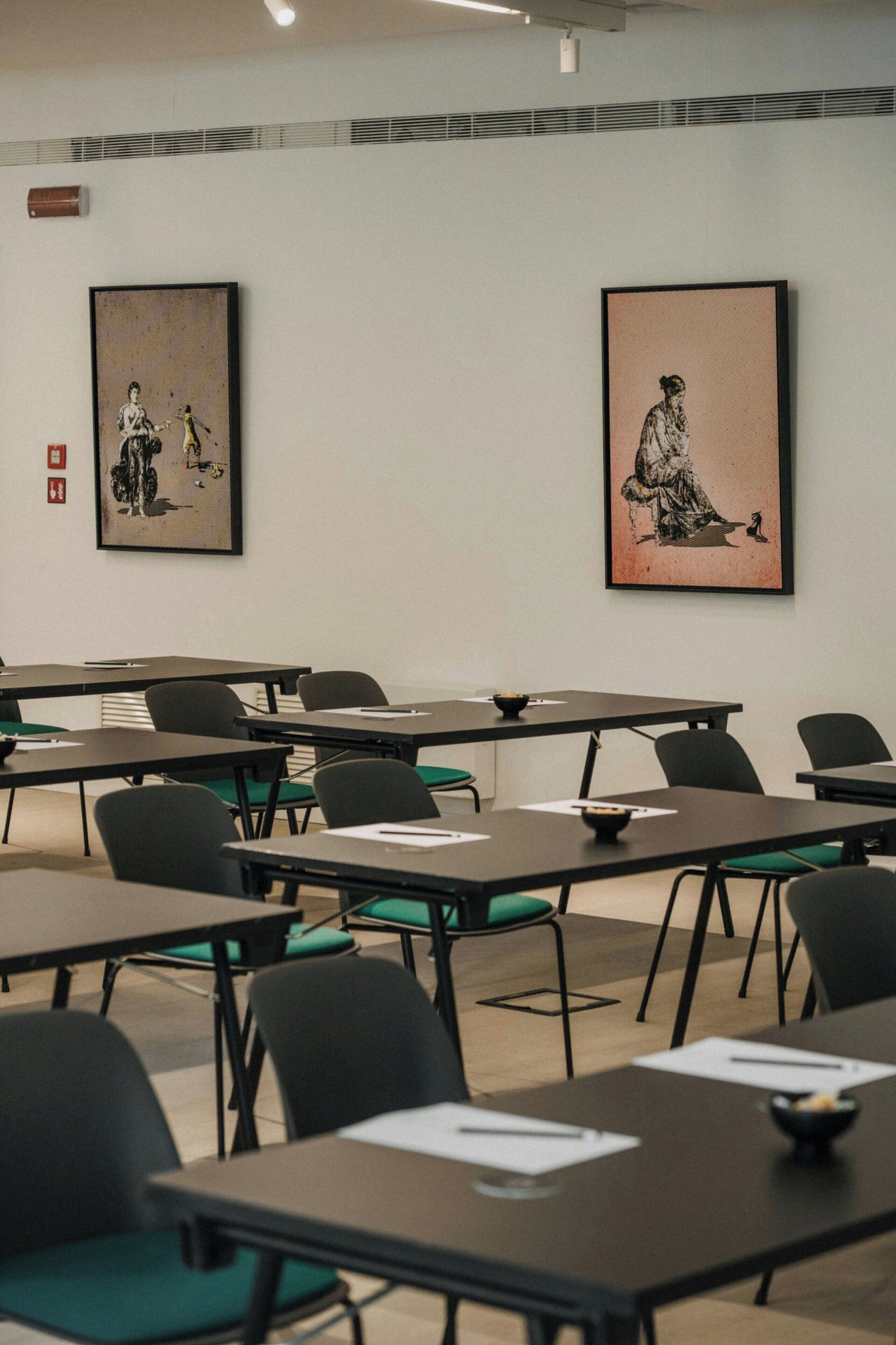 A conference room with tables and chairs, framed artwork on the walls, and a fire alarm on the left.