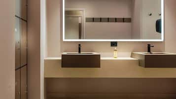 A modern bathroom with two sinks, a large mirror, and a soap dispenser.