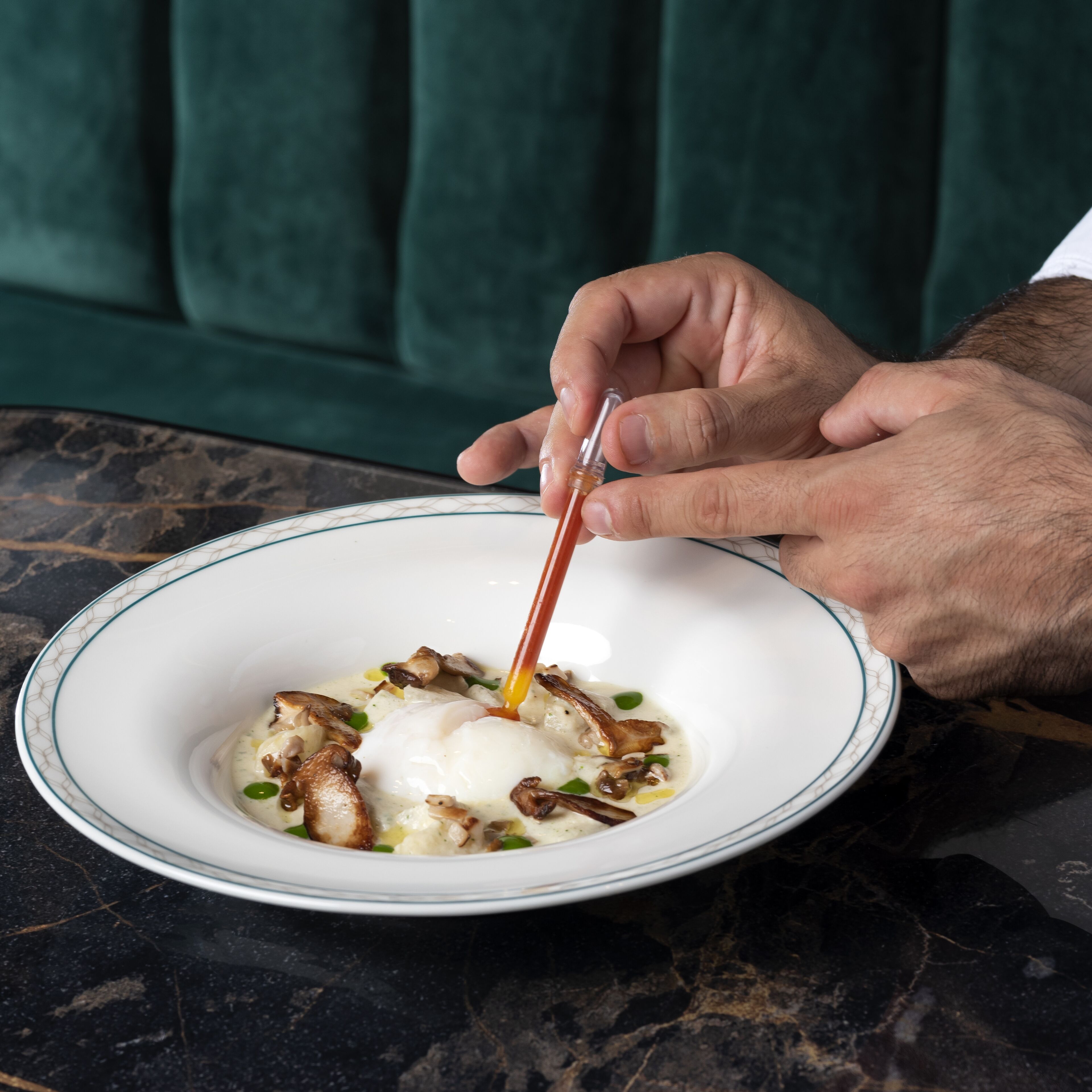 A person holding a spoon over a bowl of food with a white rim and a blue pattern.