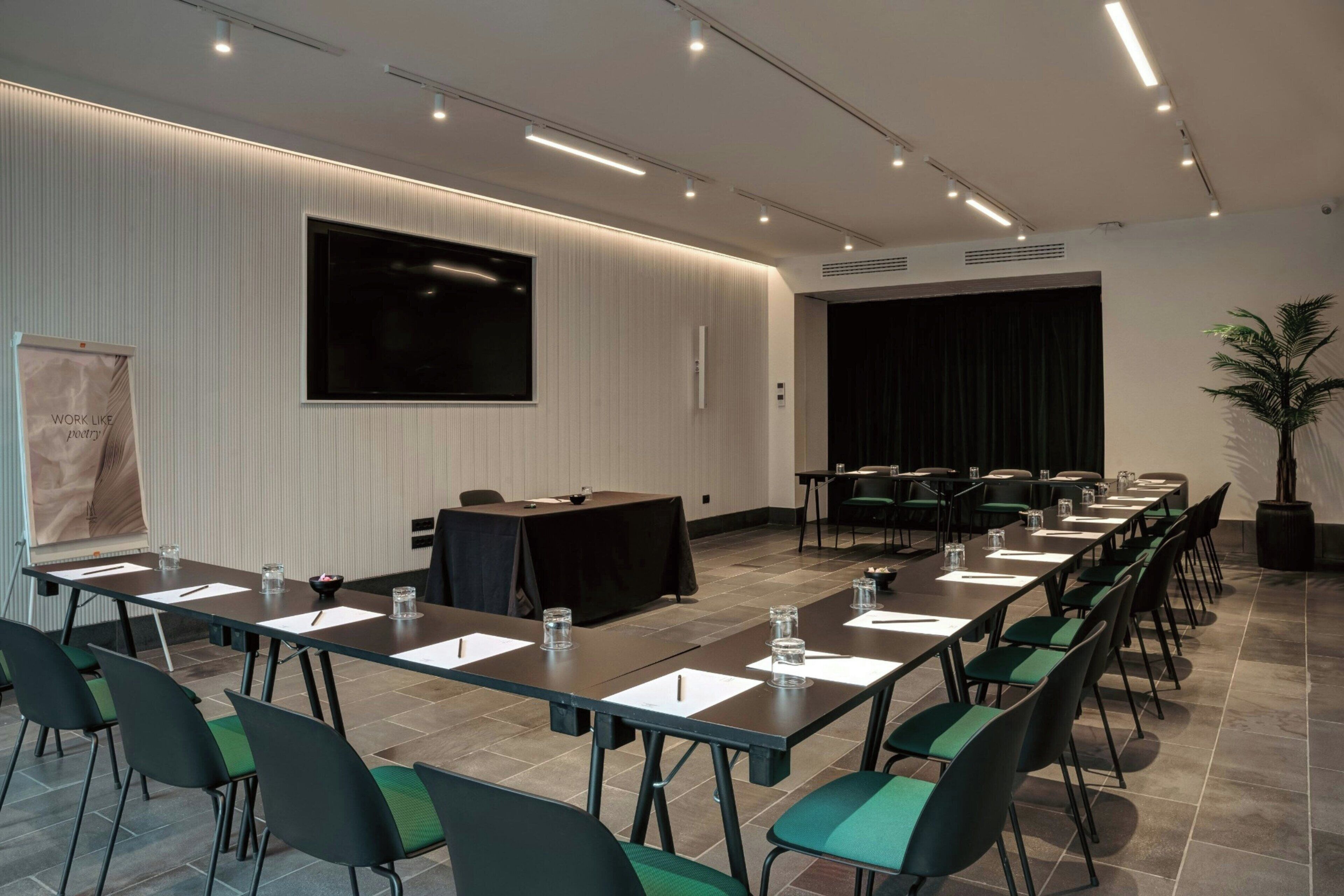Uma sala de conferências com uma mesa comprida, cadeiras, um telão e um palco.