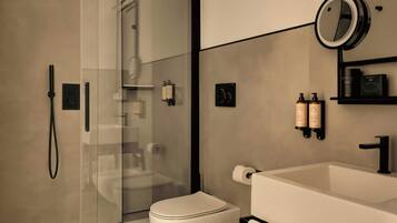 Un baño moderno con cabina de ducha de vidrio, inodoro blanco, lavabo grande con grifo negro y espejo sobre el lavabo.