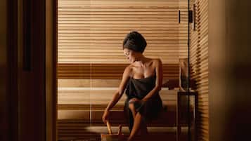 Una persona sentada en un banco en una habitación tenuemente iluminada, con listones de madera en las paredes y una pequeña mesa con un tazón y una cuchara.
