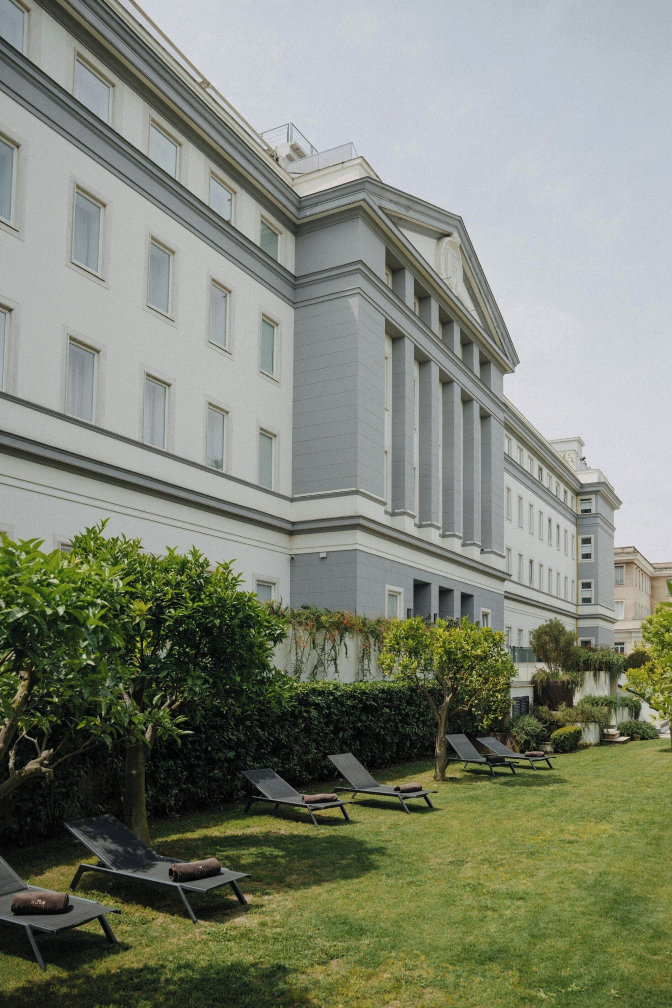 A large building with multiple windows and a well-maintained lawn with sun loungers.