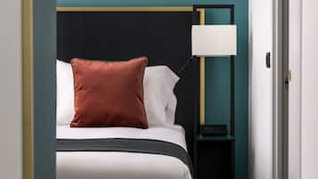 Una cama bien hecha con ropa de cama blanca y marrón, un cabecero negro y una mesita de noche con una lámpara.