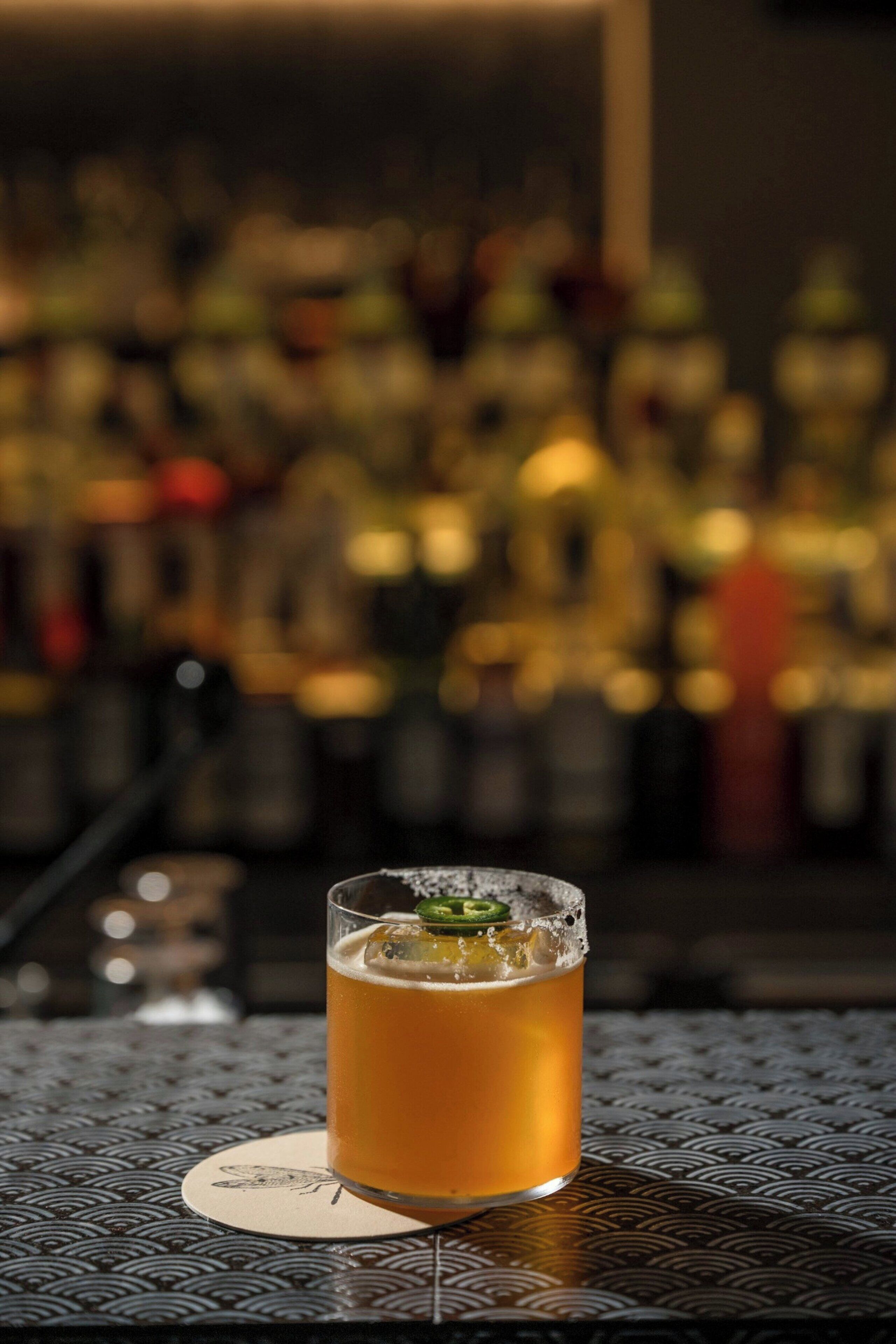 A glass of beer on a coaster with a blurred background of bottles.