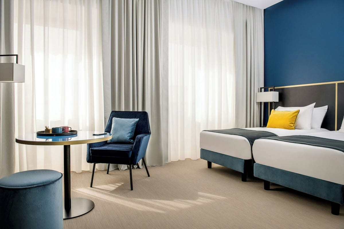 Quarto de hotel com cama, cadeira, mesa e abajur.