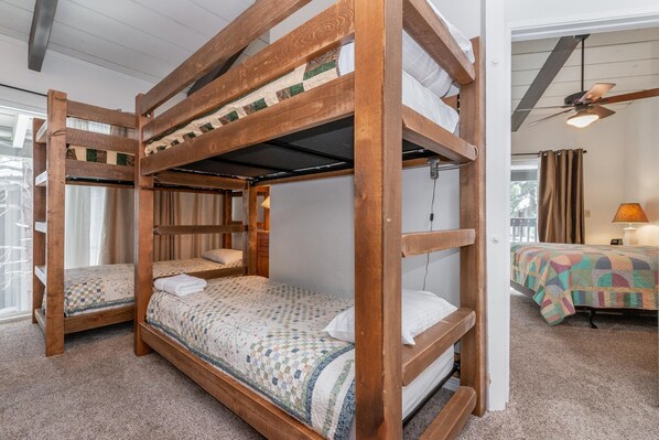 A bunk bed room with a wooden frame, a quilted bedspread, and a window with curtains. - Sierra Park Villas #66 Bldg. N (Mammoth Lakes)