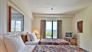 Ein Hotelzimmer mit zwei Betten, einem Fernseher, einer Lampe und einem großen Fenster mit Vorhängen.