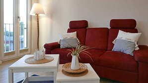 Un sofá rojo con almohadones a rayas, una lámpara blanca y una planta pequeña sobre una mesa blanca.