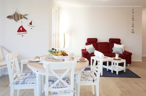 En spiseplads med et rundt bord, hvide stole og en rød sofa.