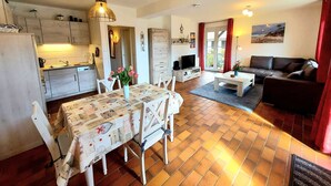 A modern apartment with a kitchen, dining area, and living room. It features a tiled floor, a dining table with chairs, a sofa, and a TV. - MeerZeit, Germany (Prerow)